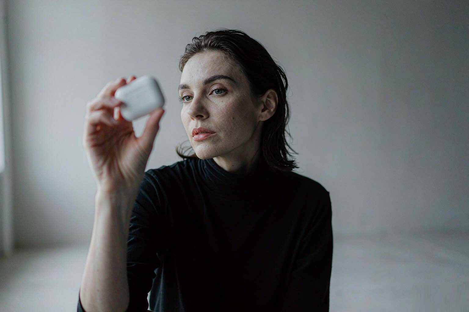 A product designer examining a wireless earbud charging case in a cool, minimal studio